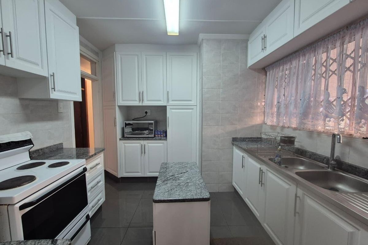 A well-maintained kitchen featuring white cabinetry, granite countertops, a double stainless steel sink, and tiled flooring with a central island unit.