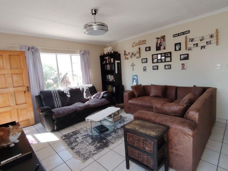 A functional living room featuring tiled flooring, a ceiling fan, and natural light from a large window.