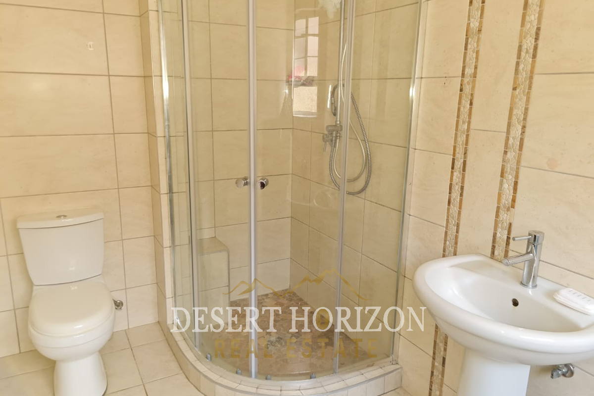 A functional bathroom featuring a corner glass shower enclosure, pedestal basin, and toilet with neutral wall and floor tiling.