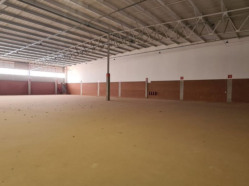 A large, open-plan industrial warehouse space featuring exposed steel roof trusses, concrete flooring, and brick wall detailing.
