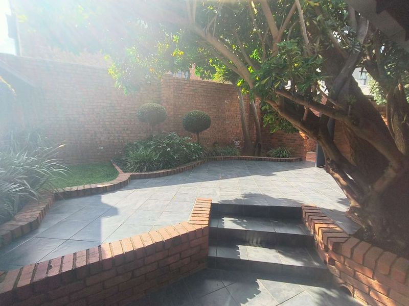 A private rear courtyard featuring a tiled patio, brick retaining walls, and established trees, providing a low-maintenance outdoor living space.