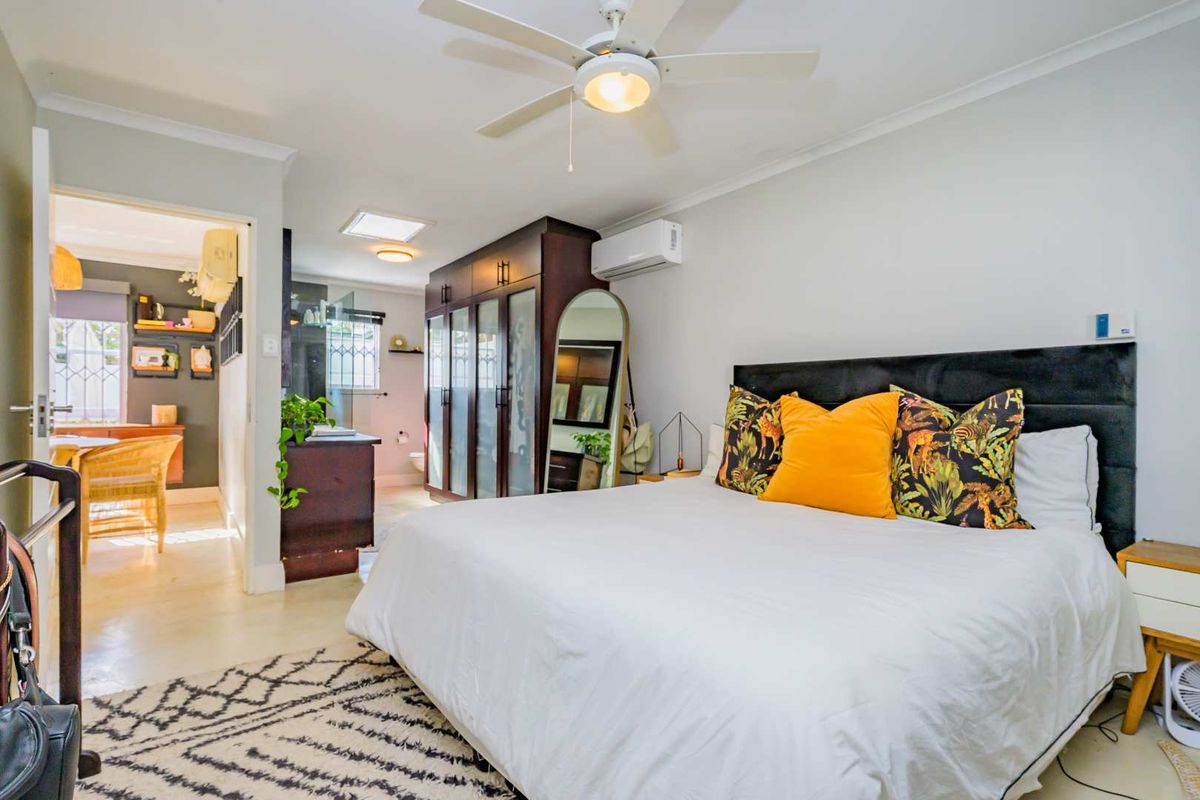 Spacious bedroom featuring built-in dark wood cabinetry, a ceiling fan, and an integrated air conditioning unit, with an adjoining en-suite bathroom area.