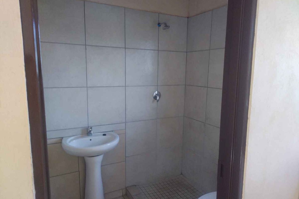 A compact bathroom featuring a pedestal basin, tiled shower enclosure, and basic plumbing fixtures.
