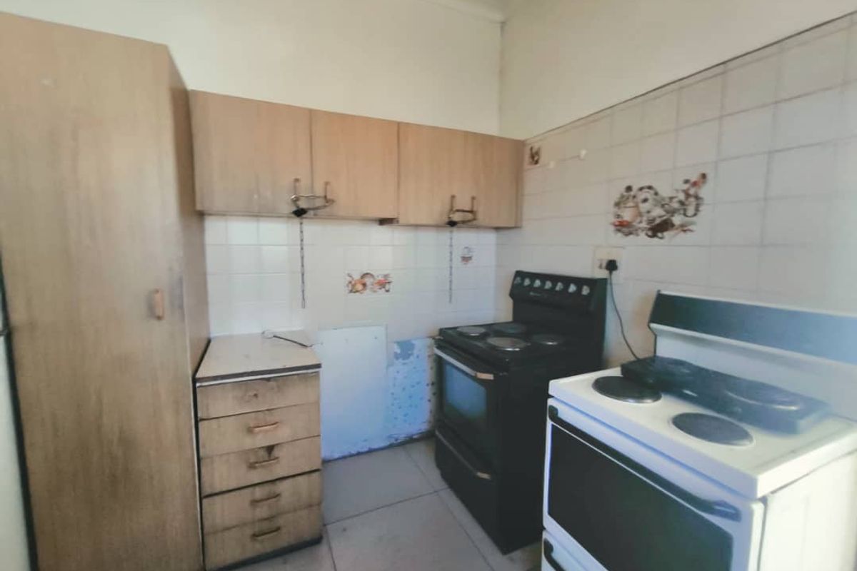 A dated kitchen featuring built-in cabinetry, tiled splashbacks, and tiled flooring, requiring cosmetic updates to modernize the space.