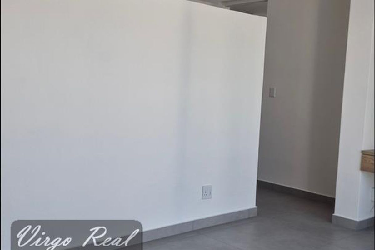 A bright, empty living area featuring modern grey floor tiles, recessed ceiling lighting, and clean white walls.