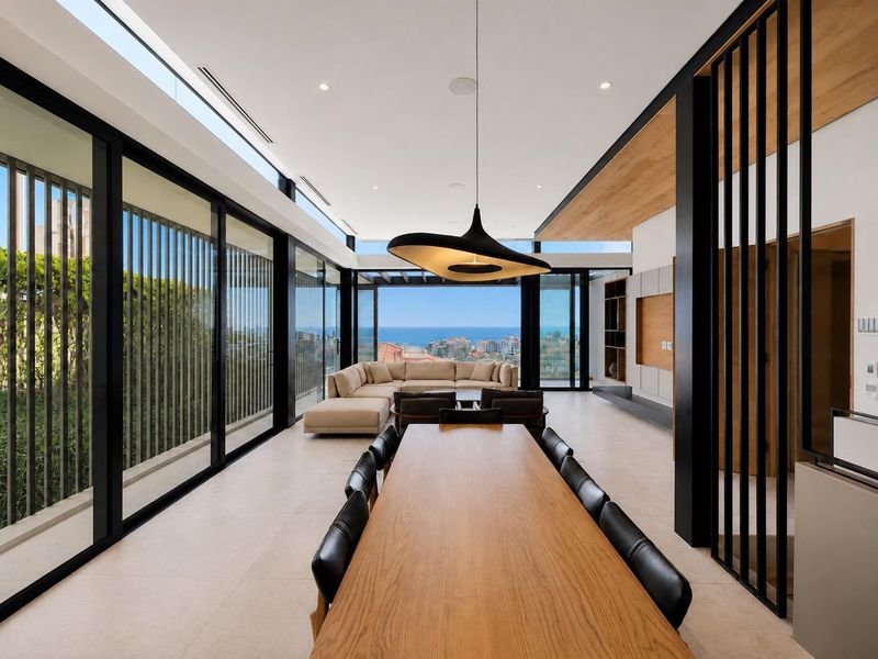 Spacious open-plan living and dining area featuring floor-to-ceiling glass walls, timber ceiling accents, and panoramic ocean views.