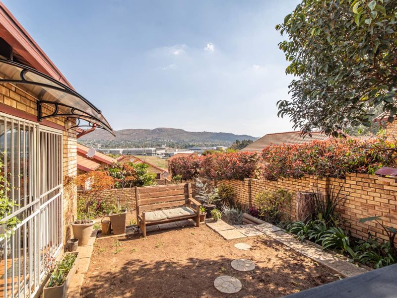 A private rear garden area featuring a brick boundary wall, paved pathway, and an awning over the entrance, offering scenic views of the surrounding area.