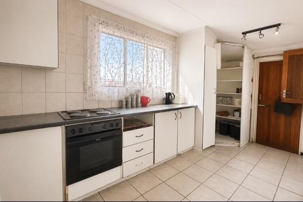 A functional kitchen featuring white cabinetry, a built-in oven with electric hob, tiled splashbacks, and a convenient walk-in pantry area.