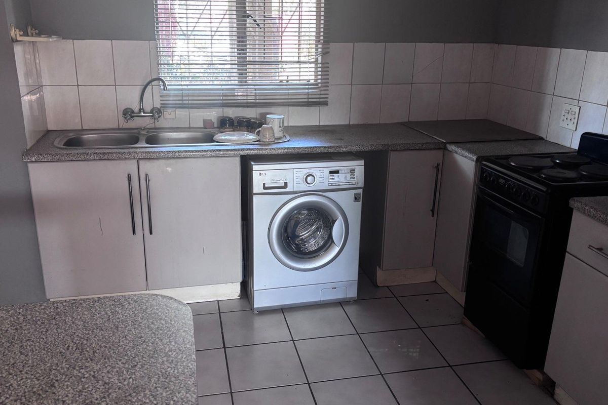 A functional kitchen featuring laminate countertops, tiled backsplash, built-in cabinetry, a double sink, and a freestanding stove with tiled flooring.