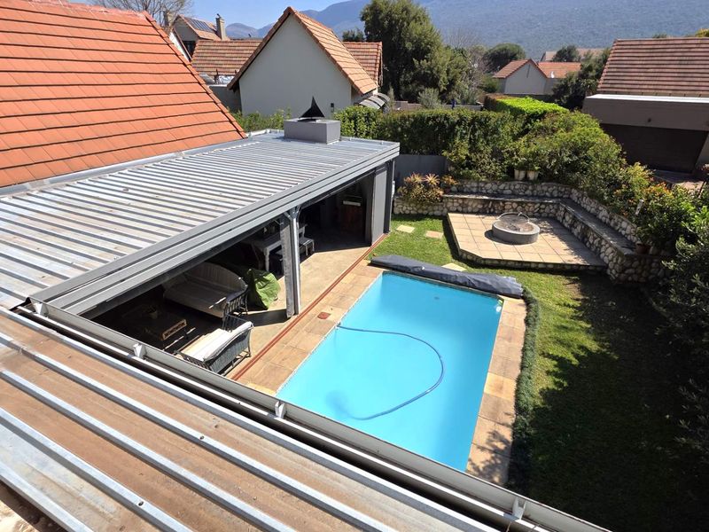 Aerial view of the rear garden featuring a swimming pool, a covered patio area, and a stone-walled fire pit section.