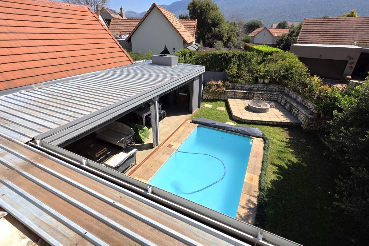 Aerial view of the rear garden featuring a swimming pool, a covered patio area, and a stone-walled fire pit section.