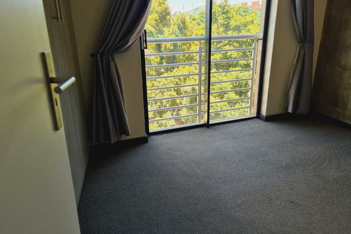 A bedroom featuring carpeted flooring and a sliding glass door that opens onto a balcony with a view of surrounding trees.