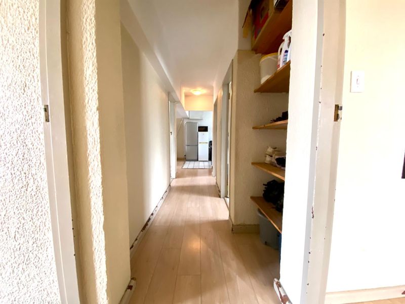 A narrow interior hallway featuring laminate flooring and built-in shelving, showing signs of wear on the skirting boards and door frames.