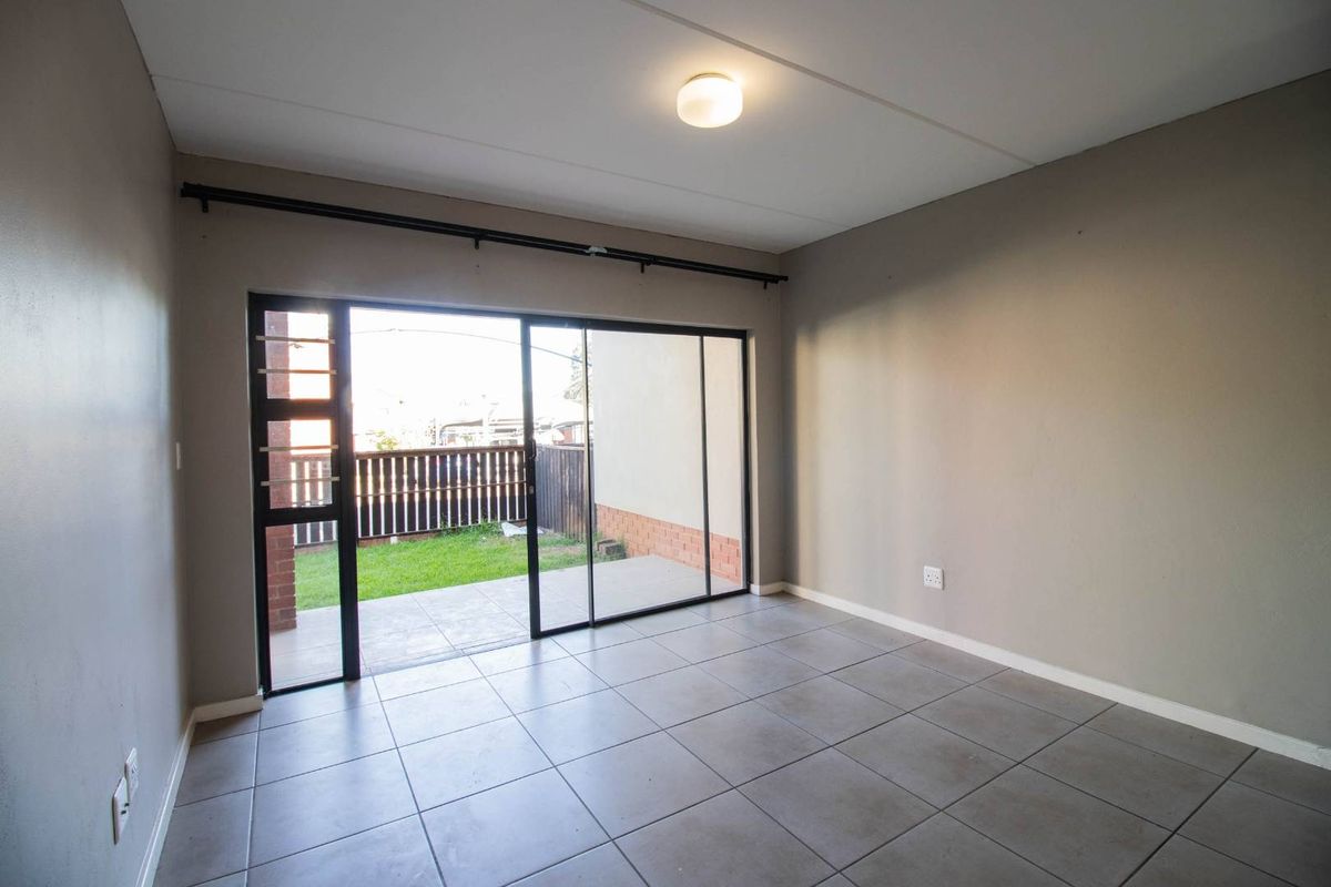 An empty living room featuring tiled flooring and large sliding glass doors that provide direct access to a private patio and garden area.