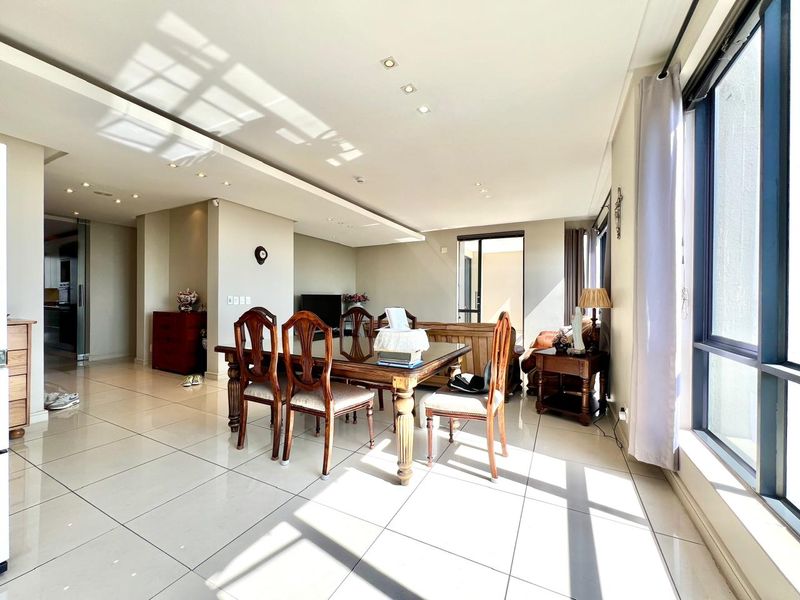 Spacious open-plan living and dining area featuring large windows, tiled flooring, and modern recessed ceiling lighting with a bright, airy atmosphere.