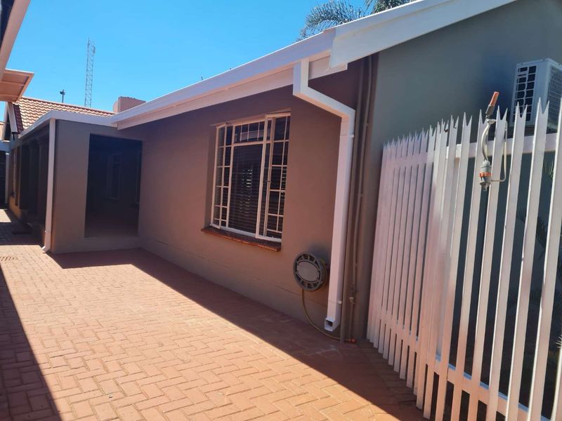 A well-maintained rear exterior area featuring paved patio flooring, security fencing, and exterior wall-mounted air conditioning unit.