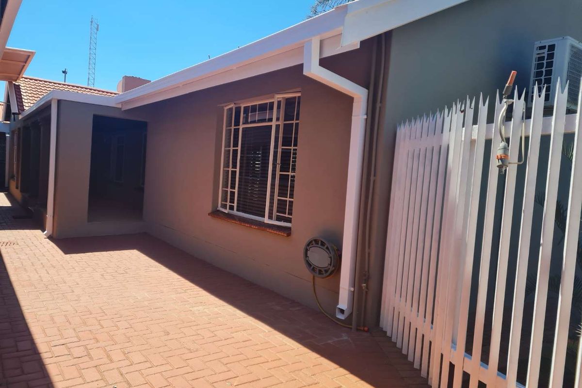 A well-maintained rear exterior area featuring paved patio flooring, security fencing, and exterior wall-mounted air conditioning unit.