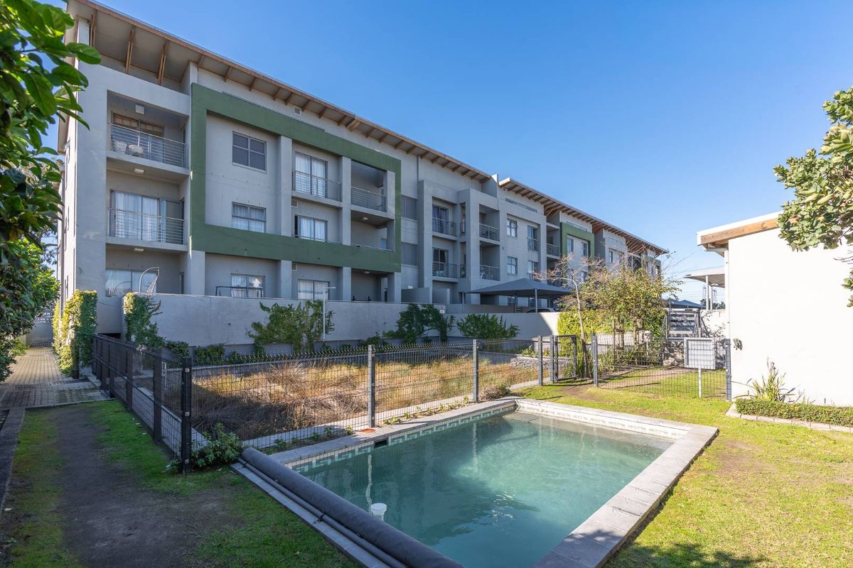 Rear view of the apartment complex featuring a swimming pool, private balconies, and a shared garden area with perimeter fencing.