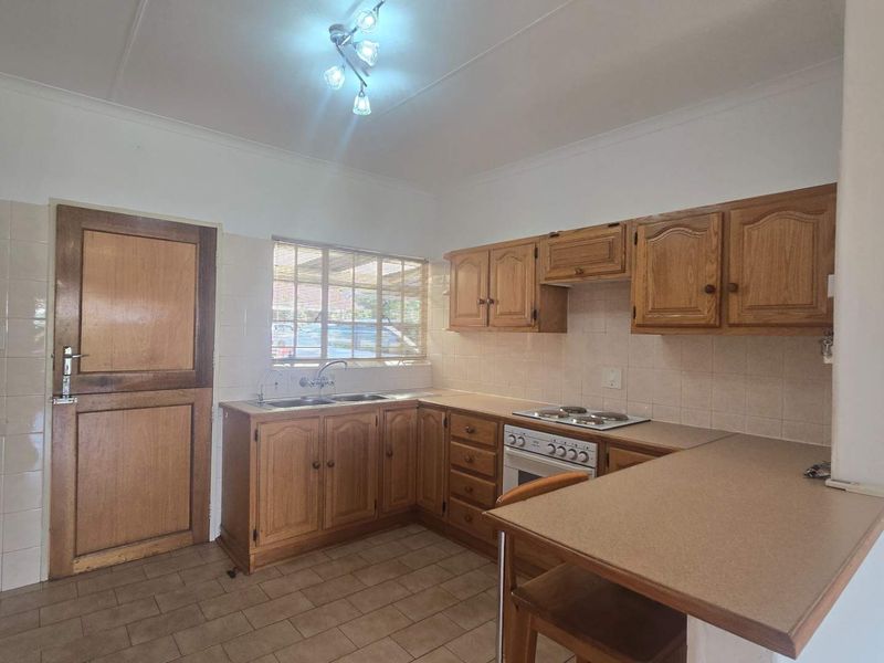 A functional kitchen featuring traditional wooden cabinetry, laminate countertops, a built-in oven with hob, and tiled flooring, offering a classic layout with ample storage.