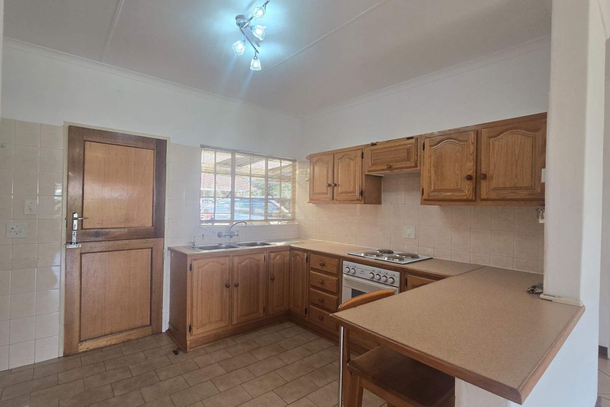 A functional kitchen featuring traditional wooden cabinetry, laminate countertops, a built-in oven with hob, and tiled flooring, offering a classic layout with ample storage.