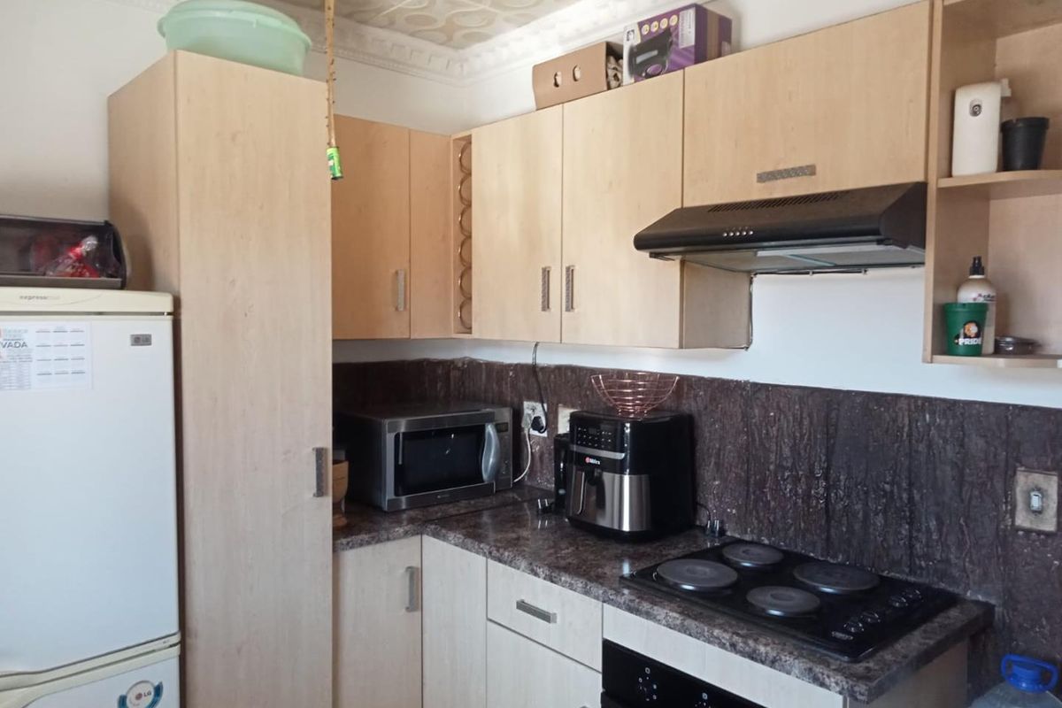 Compact kitchen featuring light wood-tone cabinetry, dark textured backsplash, integrated electric hob, oven, and extractor fan with decorative ceiling detailing.