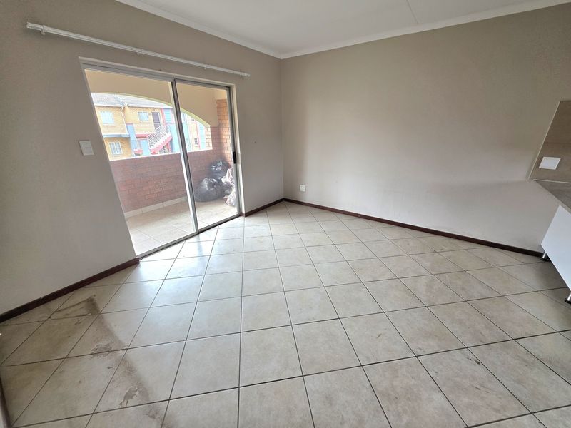 An empty open-plan living area featuring ceramic tiled flooring, neutral walls, and a sliding glass door providing access to a balcony.