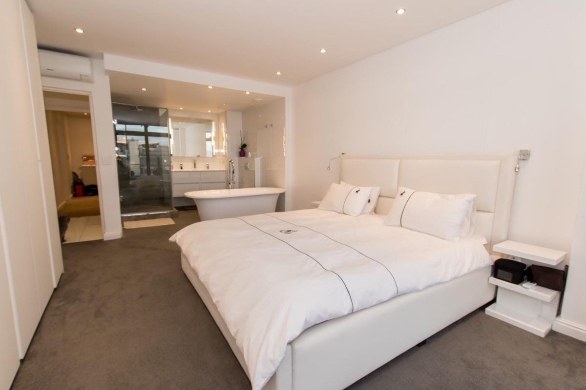 Spacious bedroom featuring an open-plan en-suite bathroom with a freestanding bathtub, glass shower, and double vanity, complemented by modern recessed lighting.