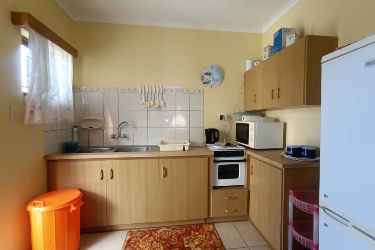 A functional kitchen featuring light wood-finish cabinetry, a built-in oven and hob, stainless steel sink, and tiled flooring.