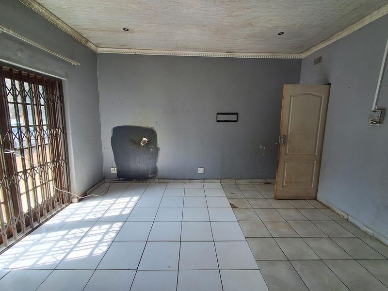 An empty living room featuring tiled flooring, security gate, and recessed lighting, requiring cosmetic updates and wall repairs to restore its appeal.