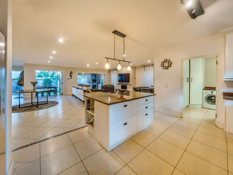 Spacious open-plan living area featuring a central kitchen island with granite countertops, tiled flooring, and seamless flow to the outdoor patio area.