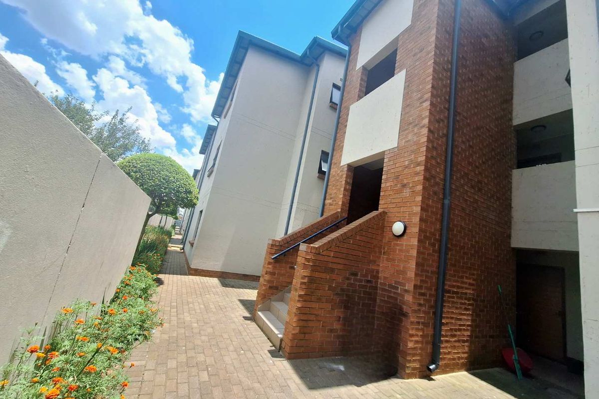 Exterior view of a townhouse complex featuring brick facade, paved walkway, and landscaped garden borders.