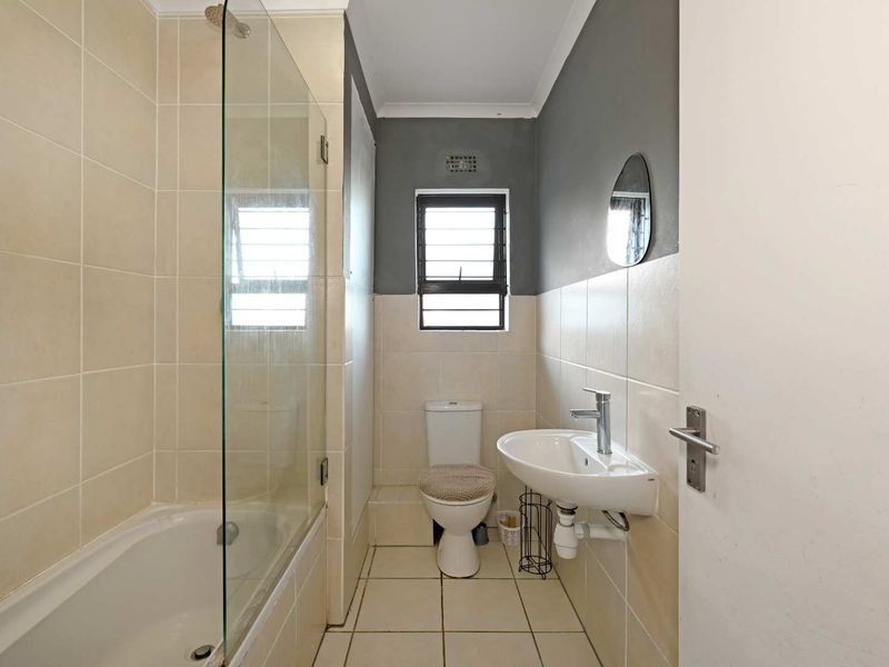 A functional bathroom featuring a bathtub with a glass screen, wall-mounted basin, and neutral tiled finishes.