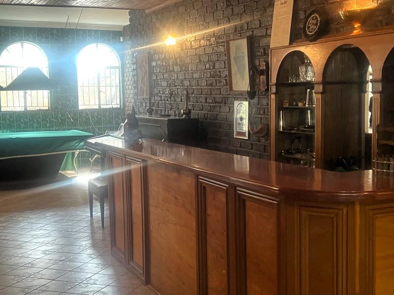 A dedicated bar area featuring a built-in wooden counter, display cabinetry, exposed brick wall, and tiled flooring with arched windows.