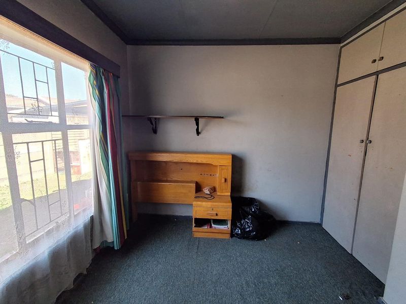 A bedroom featuring built-in wardrobes, security bars on the window, and carpet flooring, presenting a blank canvas for potential renovation and modernization.