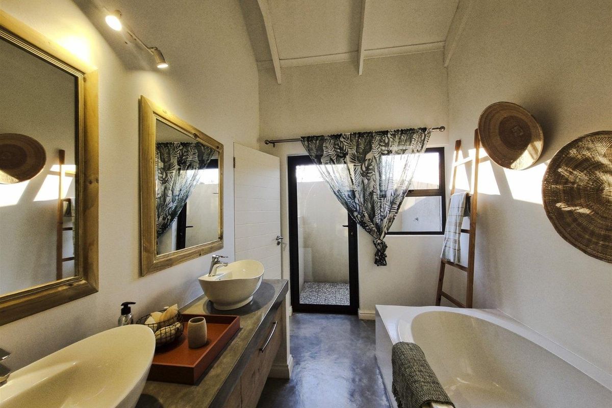 Modern bathroom featuring a double vanity with vessel sinks, a built-in bathtub, vaulted ceilings, and polished concrete flooring with direct access to an outdoor area.