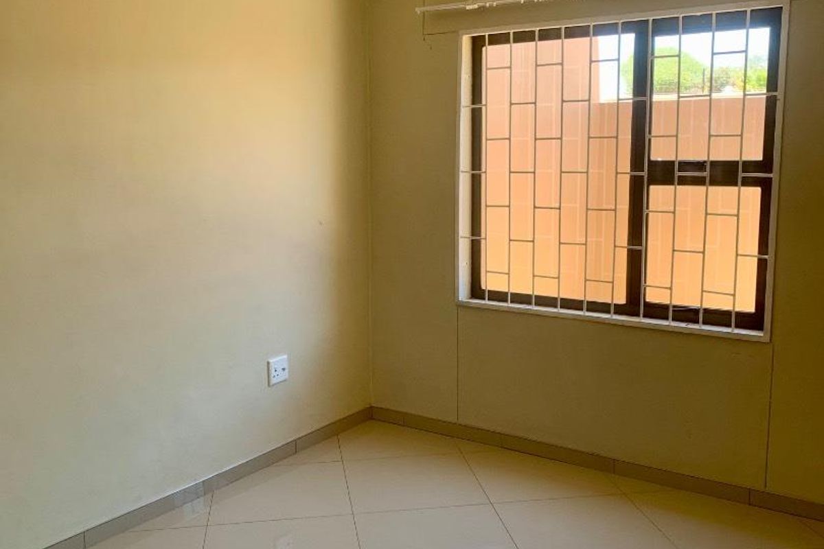 A bright, empty bedroom featuring neutral tiled flooring, a window with security bars, and a curtain rail.