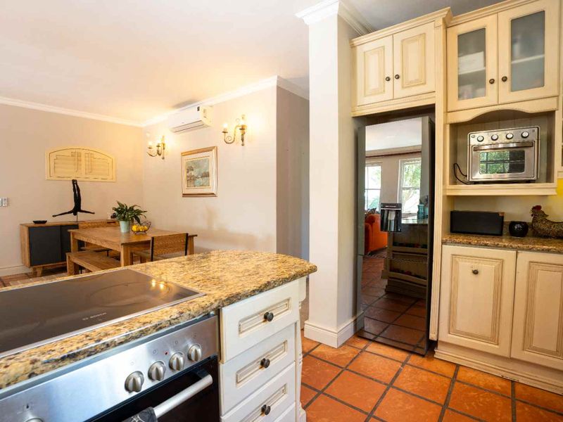 Open-plan kitchen and dining area featuring granite countertops, built-in cabinetry, integrated appliances, and terracotta floor tiles, creating a warm and functional living space.