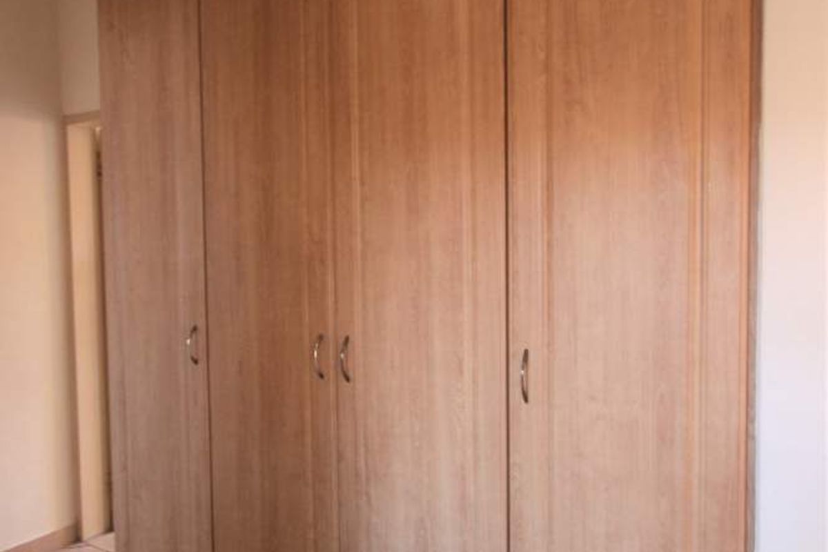 A bedroom featuring light wood-finish built-in cupboards and neutral tiled flooring, offering a clean and functional storage solution.