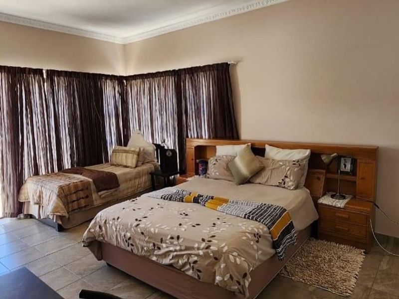 Spacious bedroom featuring tiled flooring, decorative ceiling cornices, and a built-in wooden headboard with integrated bedside storage.