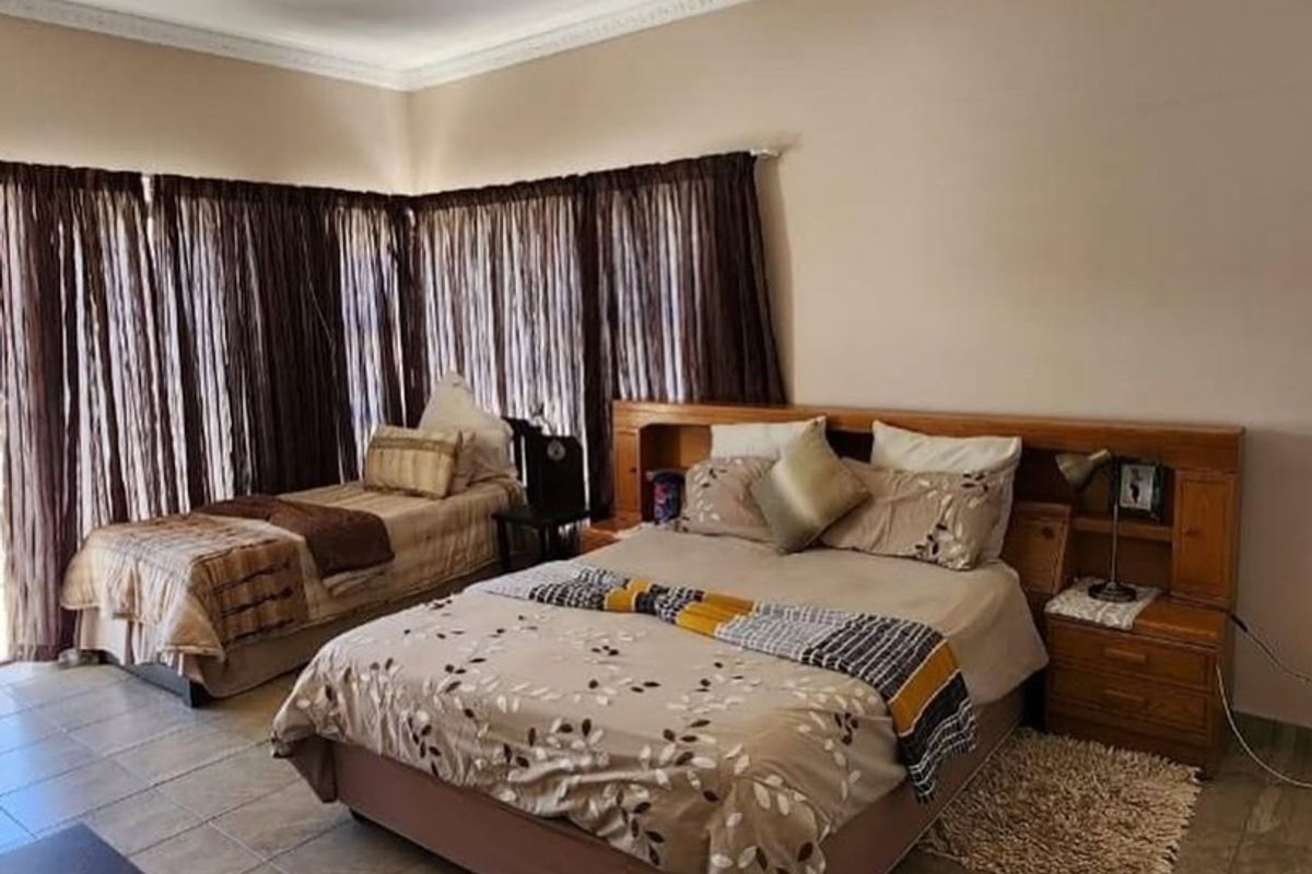 Spacious bedroom featuring tiled flooring, decorative ceiling cornices, and a built-in wooden headboard with integrated bedside storage.