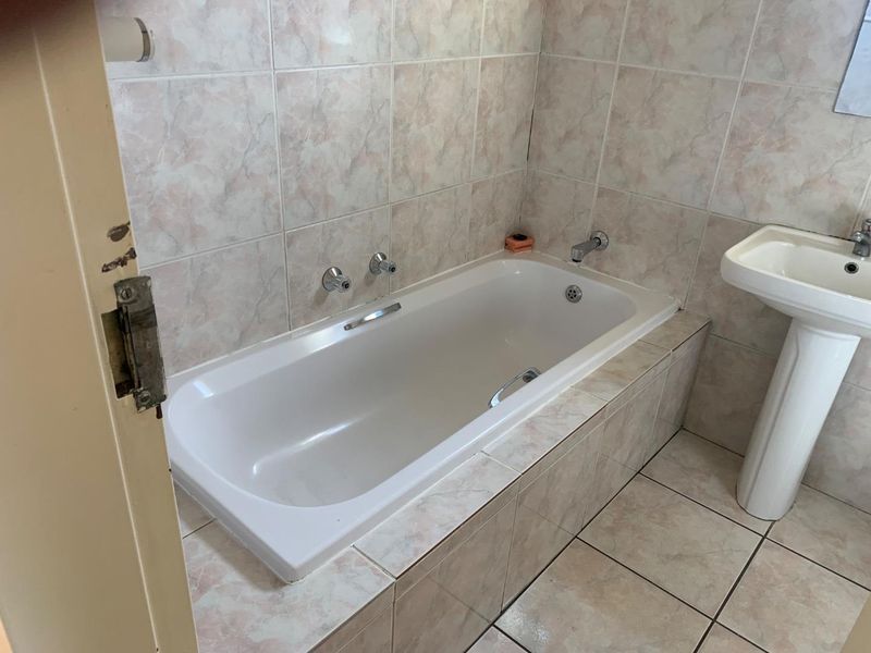 A functional bathroom featuring a built-in bathtub with tiled surround and a pedestal basin, finished with neutral ceramic wall and floor tiles.