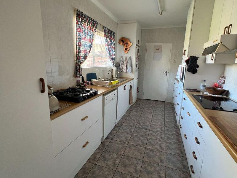 A functional galley-style kitchen featuring dual cooking surfaces, ample built-in cabinetry, tiled flooring, and a tiled backsplash.