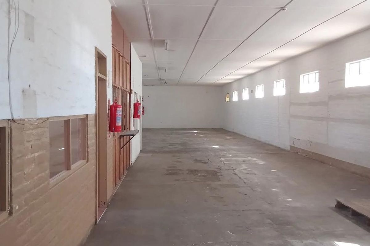 A spacious, empty industrial utility area featuring concrete flooring, exposed brick walls, and multiple windows providing natural light.