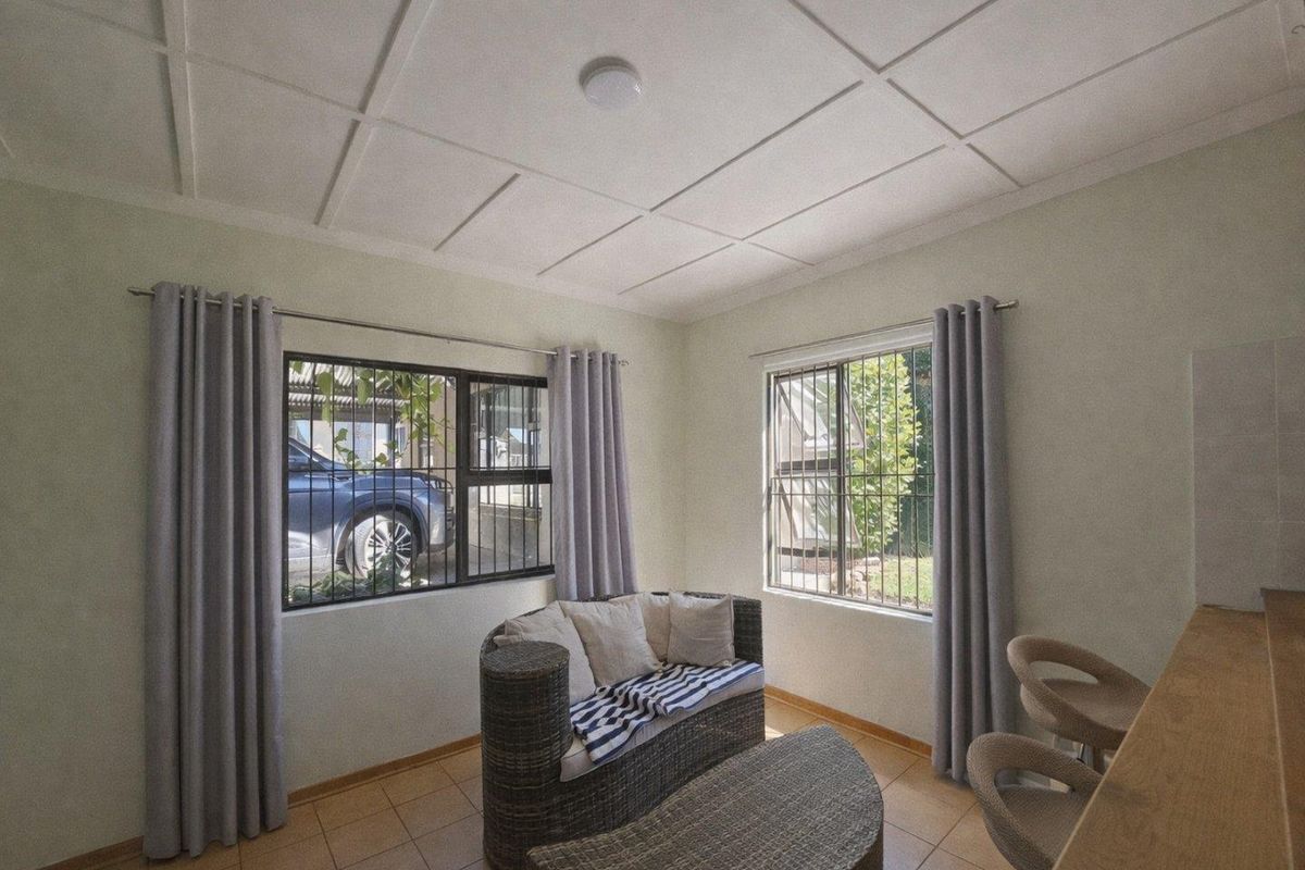 A bright living area featuring tiled flooring, a grid-patterned ceiling, and security bars on the windows.