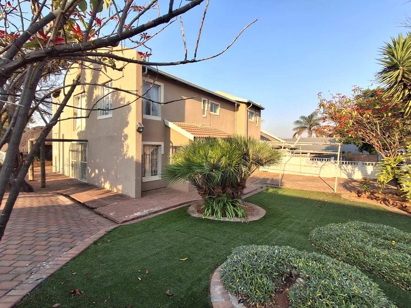 Rear view of the property featuring a paved patio area, artificial lawn, and established garden landscaping with a brick boundary wall.