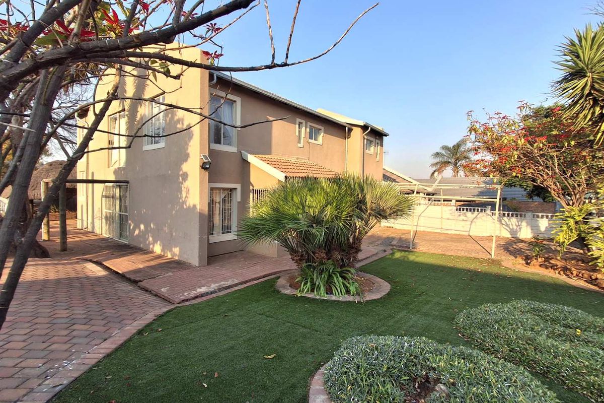 Rear view of the property featuring a paved patio area, artificial lawn, and established garden landscaping with a brick boundary wall.
