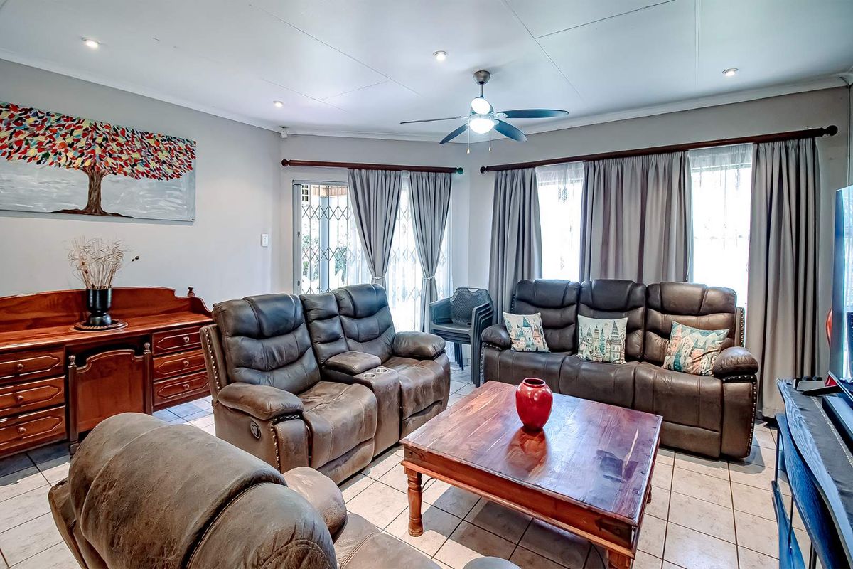 A comfortable living room featuring tiled flooring, recessed downlighting, a ceiling fan, and sliding glass doors with security gates leading to the exterior.