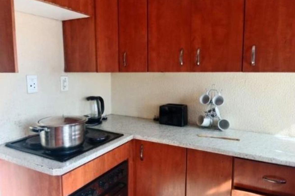 A compact kitchen featuring wooden cabinetry, a light-toned laminate countertop, and a built-in electric hob and oven setup.