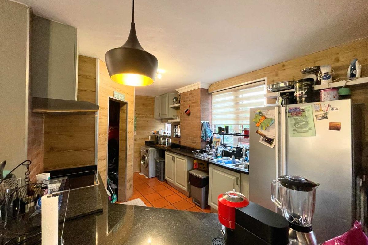 A functional kitchen featuring granite countertops, wood-paneled walls, tiled flooring, and built-in cabinetry with an integrated extractor fan.