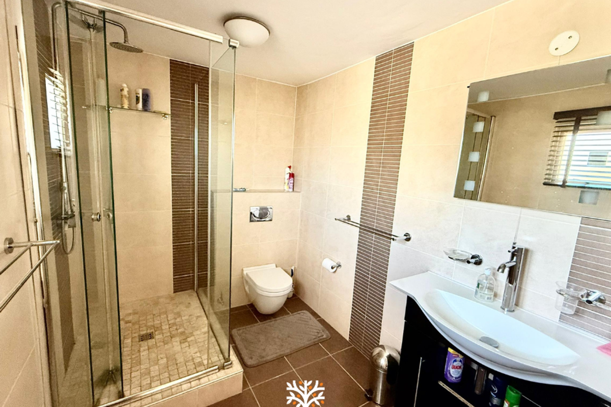 Modern bathroom featuring a glass-enclosed shower, wall-mounted toilet, and a contemporary vanity with a basin, finished with neutral wall and floor tiling.